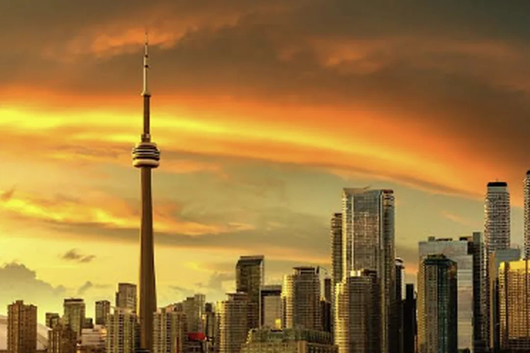 Perfil de una ciudad al atardecer con una torre alta y nubes anaranjadas