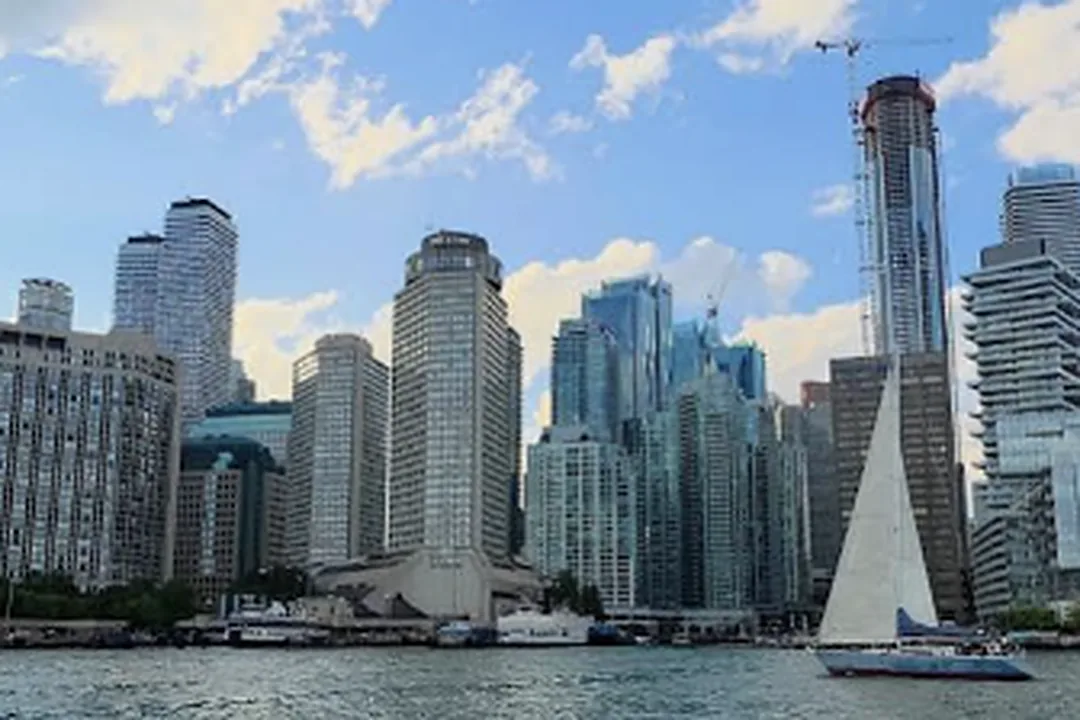 Velero navegando frente a edificios altos en la orilla de un lago en un día soleado